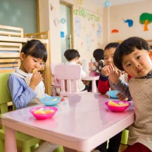 Kids seated around a table in a colorful classroom, eating snacks happily.