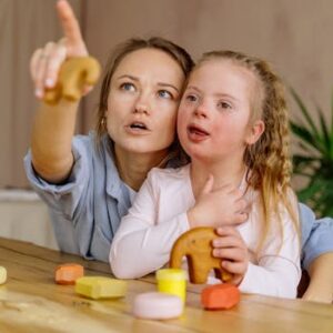 Woman and girl with Down syndrome engaging in play and learning together indoors.