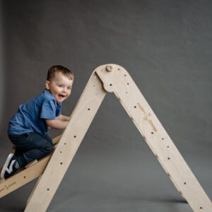 A cheerful young boy in blue shirt climbing a wooden ladder indoors.